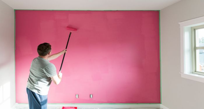 man using roller to paint room wall