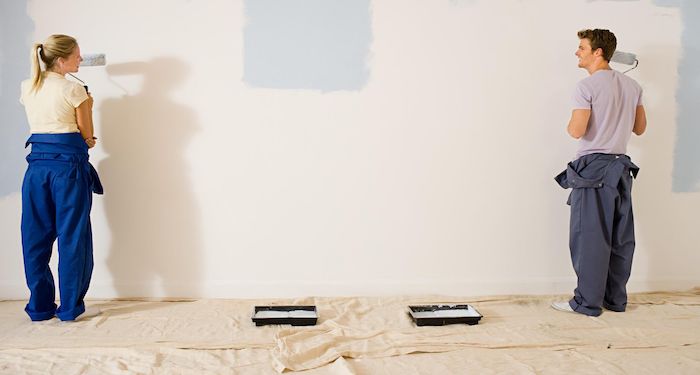 Man and woman in blue overalls painting wall