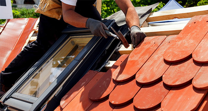 man on ladder fixing roof tile by skylight