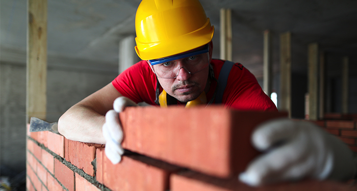 workman in yellow hard hat building a wall