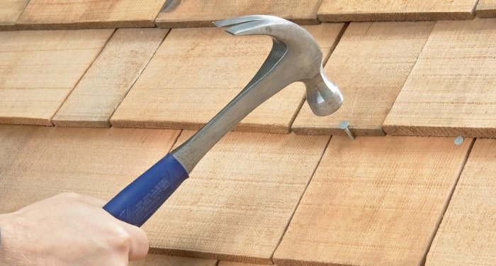 person hammering nail in to wood tile