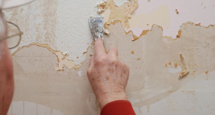 man removing wallpaper with scrapper